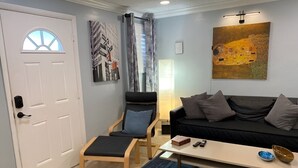 Una sala de estar con sofá, sillón, mesa de centro, alfombra, puerta y un cuadro en la pared.
