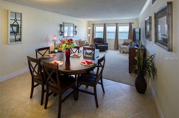 A dining area with a round table, chairs, and a vase with flowers. There is a view of the ocean through large windows. - Spectacular Gulf-Front Fully Renovated 2B/2B In Sand Key,Clearwater Beach,FL (Clearwater Beach)