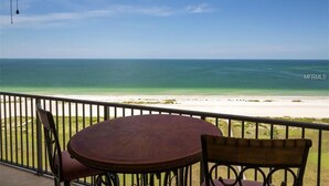 Un balcon avec une table ronde et des chaises, donnant sur une plage et offrant une vue dégagée sur l’océan.