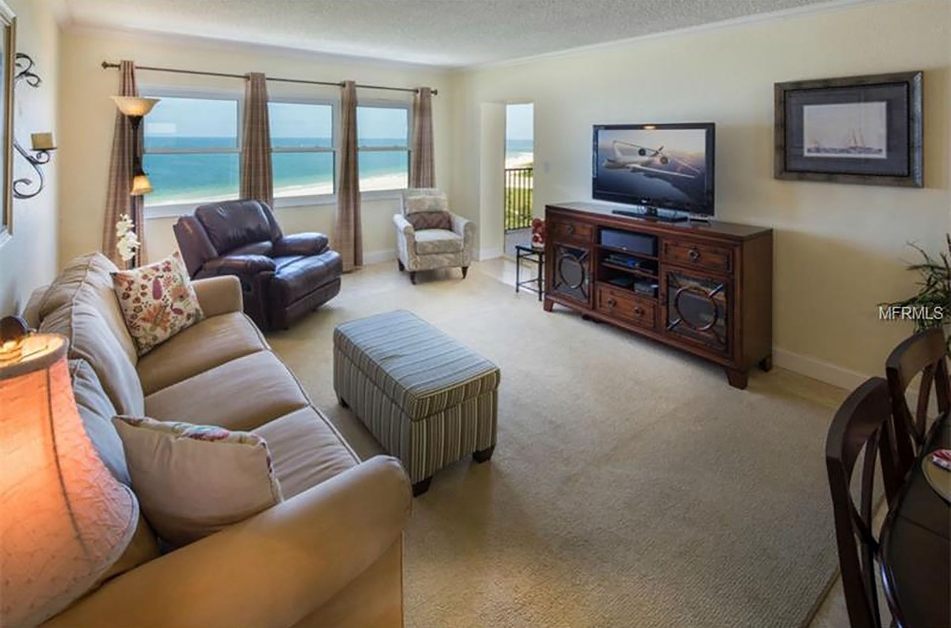 A living room with a large window overlooking the ocean, a leather sofa, a television, and a wooden cabinet.