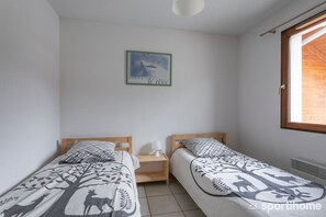 A bedroom with two single beds, a nightstand, a wall-mounted picture, and a window with a wooden blind. - New apartment, near the ski resorts, due south, beautiful view of Risoul. (Guillestre)