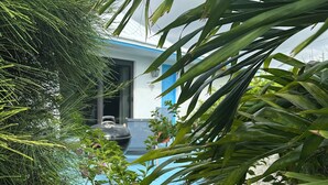 Un rigoglioso giardino con vivaci fiori rosa e verdeggiante vegetazione, che conduce a un edificio con facciata blu e bianca.