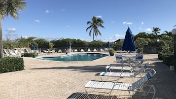 A pool area with lounge chairs and umbrellas, surrounded by palm trees and a stone wall.