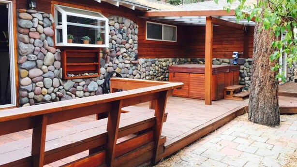 Un chalet rustique avec un mur en pierre, une terrasse en bois et un jacuzzi.
