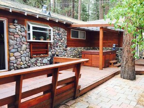 A rustic cabin with a stone wall, wooden deck, and a hot tub. - Come Enjoy Tranquility In The Forest In Tahoe (Stateline)