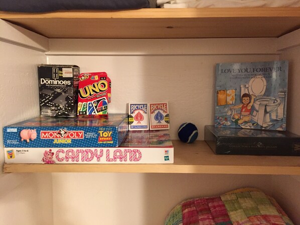 A shelf with various board games including Dominoes, UNO, Monopoly Junior, Candy Land, Bicycle, and a book titled 'Love You Forever'. - Come Enjoy Tranquility In The Forest In Tahoe (Stateline)