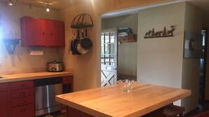 Una cocina con encimeras de madera, lavavajillas y un armario rojo. Se observa una isla de madera con un bol de vidrio.