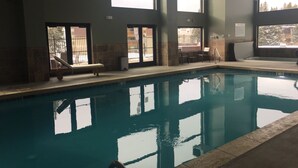 Una piscina interior con agua cristalina, sillas de descanso y grandes ventanales que ofrecen vistas al exterior.