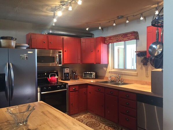 Una cocina con armarios rojos, electrodomésticos de acero inoxidable, encimera de madera y ventana con vistas.