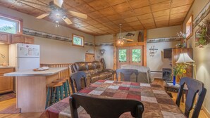 Ein gemütliches Blockhäuschen-Interieur mit Holzbalkendecke, einem Esstisch mit gestepptem Tischläufer, einer Ledersofa und einer Bar.