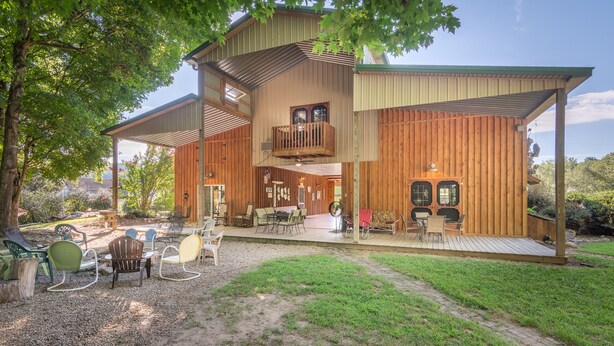 Ein zweistöckiges Holzhaus mit einer Veranda, Sitzgelegenheiten im Freien und einer kleinen Terrasse.