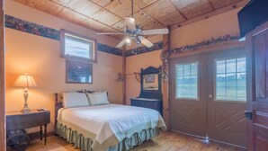 Ein Schlafzimmer mit einem Bett, einem Nachttisch, einer Lampe, einem Deckenventilator und einer Tür mit Fenstern.