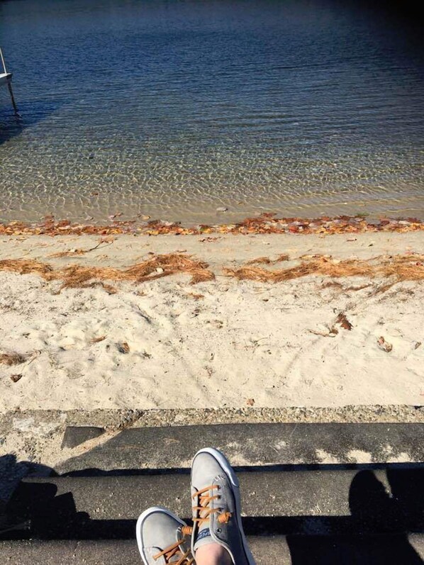 A pair of sneakers on a concrete ledge overlooking a body of water with clear water and a sandy beach.