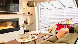 Un salon chaleureux avec une cheminée, des fauteuils confortables et un coin repas avec une table mise pour deux personnes.
