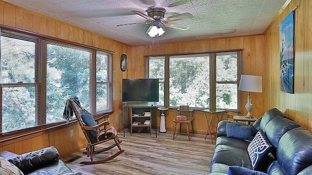 A cozy living room with wooden walls, a ceiling fan, a TV, a rocking chair, and a leather sofa. - Smoky Mountain Getaway. Enjoy Seclusion,Views,Motorcycling, Shops w Paved Access (Franklin)