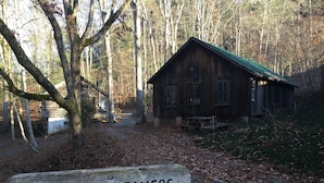 A rustic wooden cabin with a green roof, surrounded by trees and a gravel path. A wooden sign in front reads "NONAH WEAVERS". - Smoky Mountain Getaway. Enjoy Seclusion,Views,Motorcycling, Shops w Paved Access (Franklin)