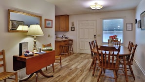 A dining area with a wooden table and chairs, a wooden desk with a lamp, and a window with blinds. - Smoky Mountain Getaway. Enjoy Seclusion,Views,Motorcycling, Shops w Paved Access (Franklin)