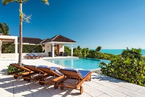 Ein Poolbereich mit Liegestühlen, einer überdachten Sitzgelegenheit und Meerblick.