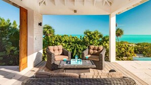 A covered outdoor seating area with wicker furniture and a view of the ocean. - Beachfront Villa w/ Infinity Pool & Ocean Views (Long Bay)
