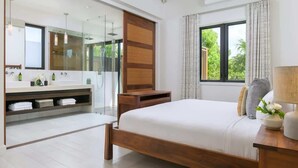 A modern bedroom with a large bed, a wooden bedside table, a nightstand, a built-in wardrobe, a large mirror, and a bathroom with a glass shower enclosure. - Beachfront Villa w/ Infinity Pool & Ocean Views (Long Bay)