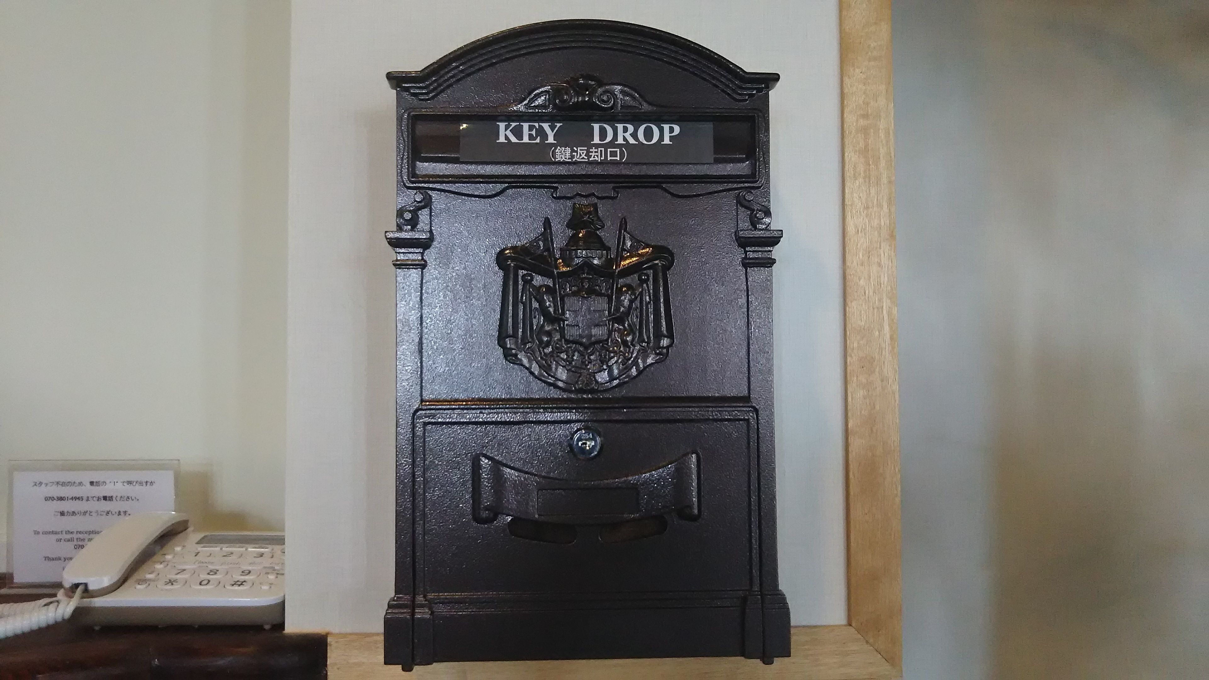 A black key drop mailbox with a crest emblem and a sign reading "KEY DROP".