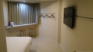 A small hotel room with a bed, a window with curtains, a TV mounted on the wall, and two stools. - HOTEL Sunset Marino - Adults Only (Chatan)