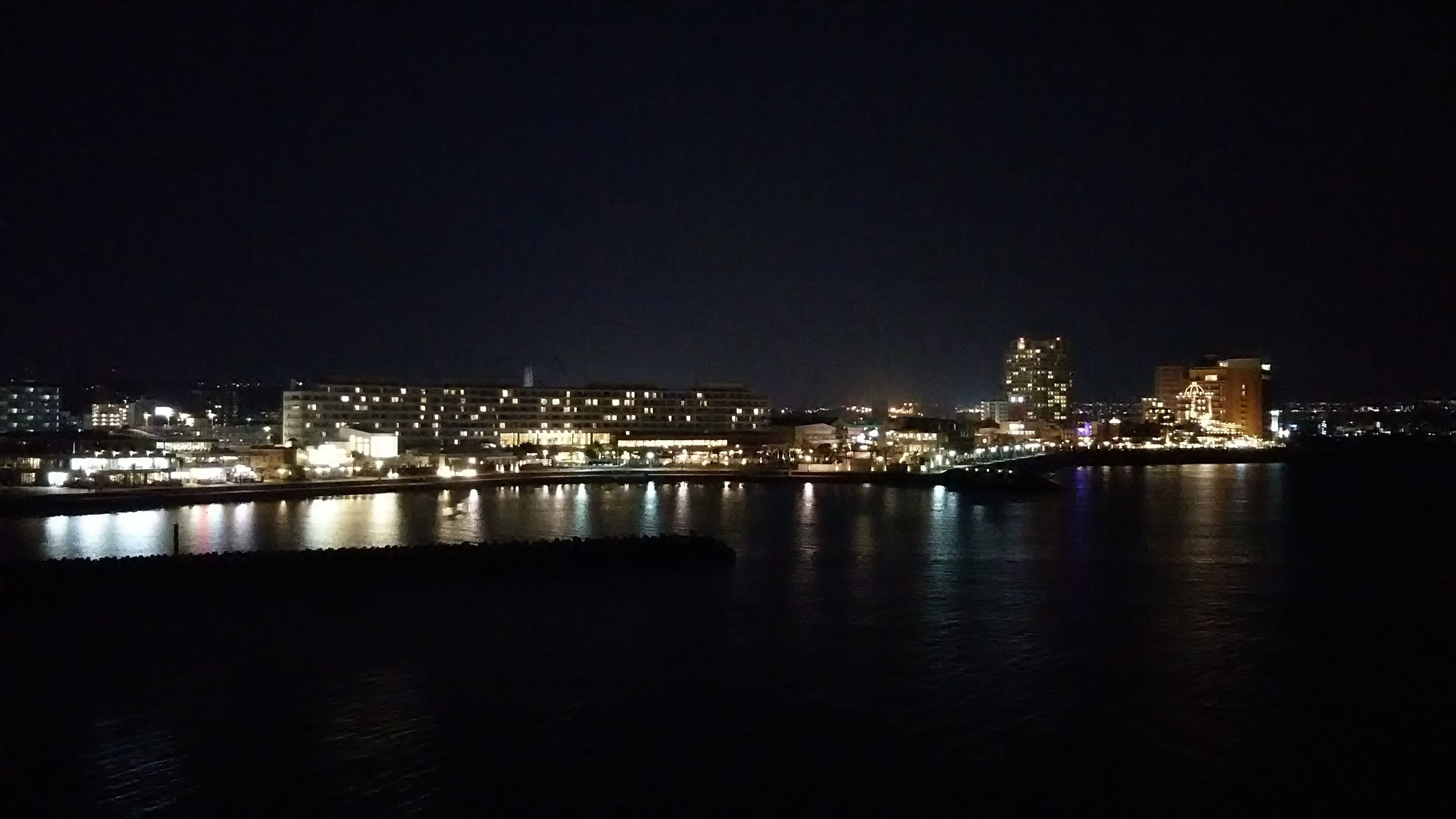 A nighttime cityscape with illuminated buildings along a waterfront.