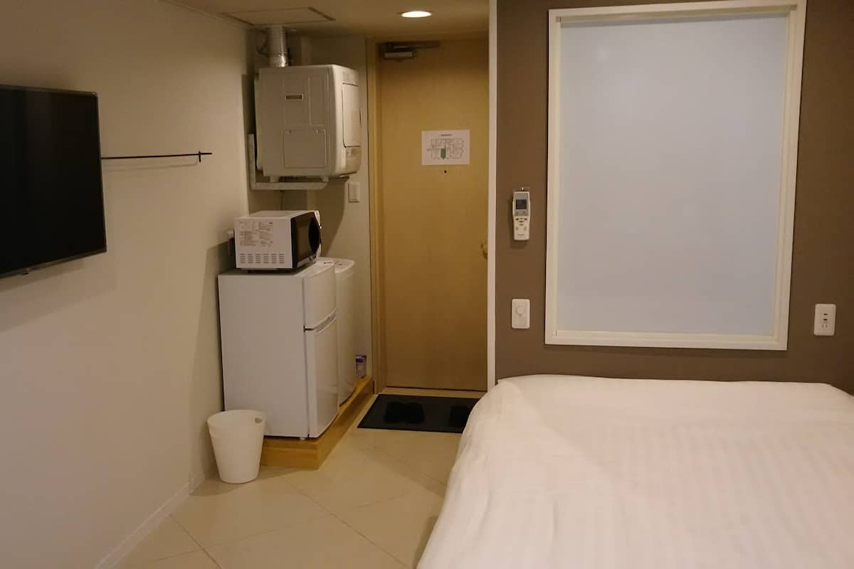 Een hotelkamer met een bed, een aan de muur bevestigde televisie, een magnetron en een koelkast.