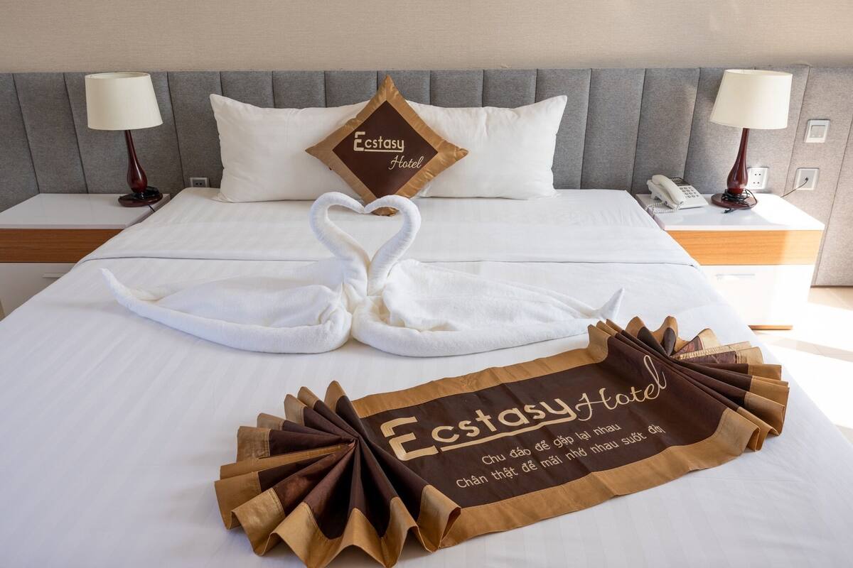 A neatly made bed with a heart-shaped towel arrangement and a welcome sign.