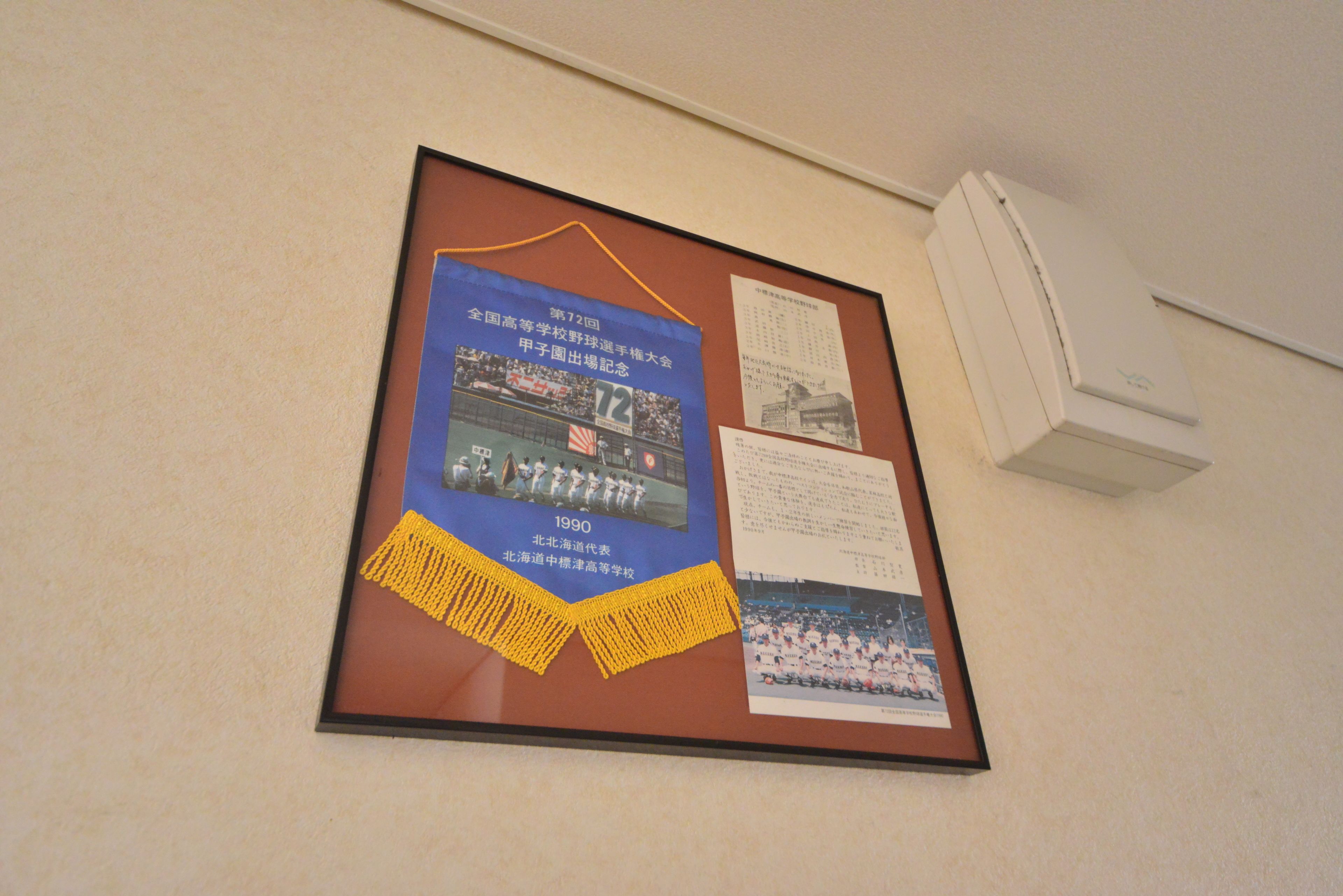 A bulletin board with framed pictures and text, a white air conditioning unit, and a beige wall.