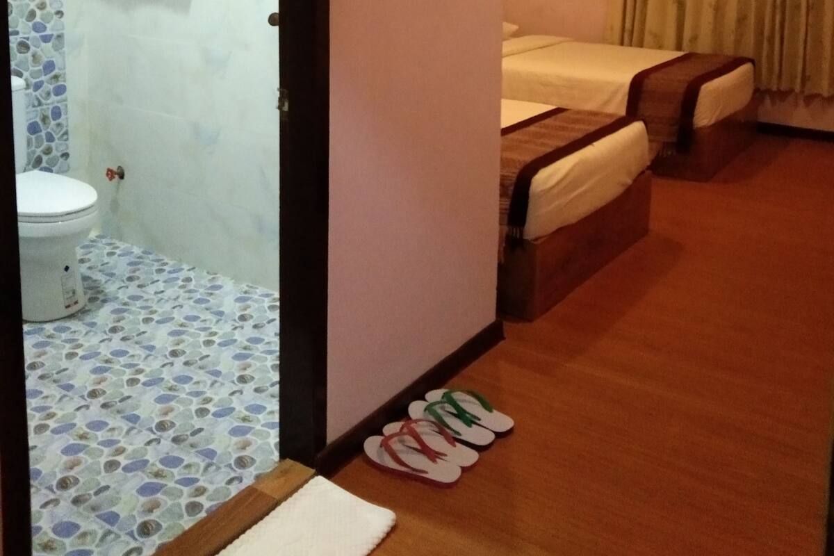 Une chambre d’hôtel avec une salle de bain, un lit, une douche et des chaussons sur le sol.