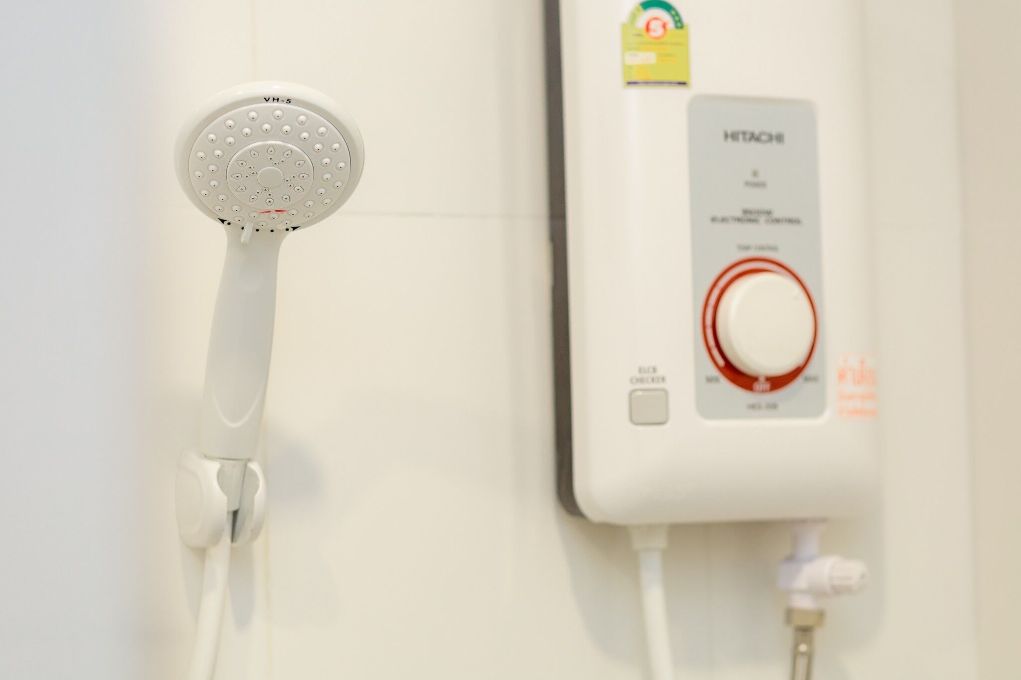 Un cabezal de ducha blanco y un panel de control montado en la pared con una perilla roja y un botón.