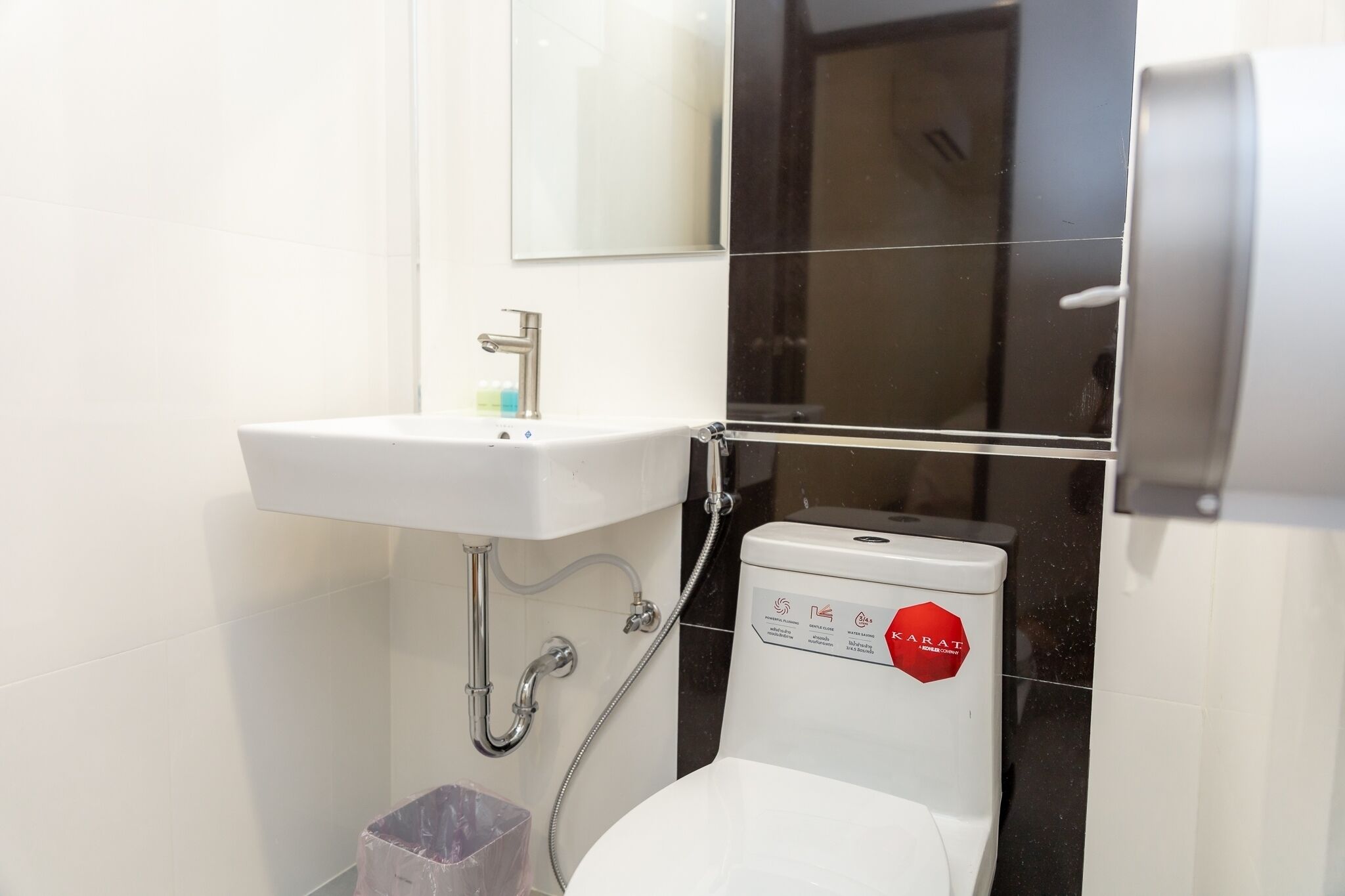 A bathroom with a white sink, a mirror, and a toilet with a red sticker.