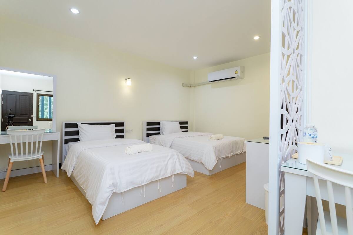 Habitación de hotel con dos camas, un escritorio, una silla, una mesita pequeña y un aire acondicionado.