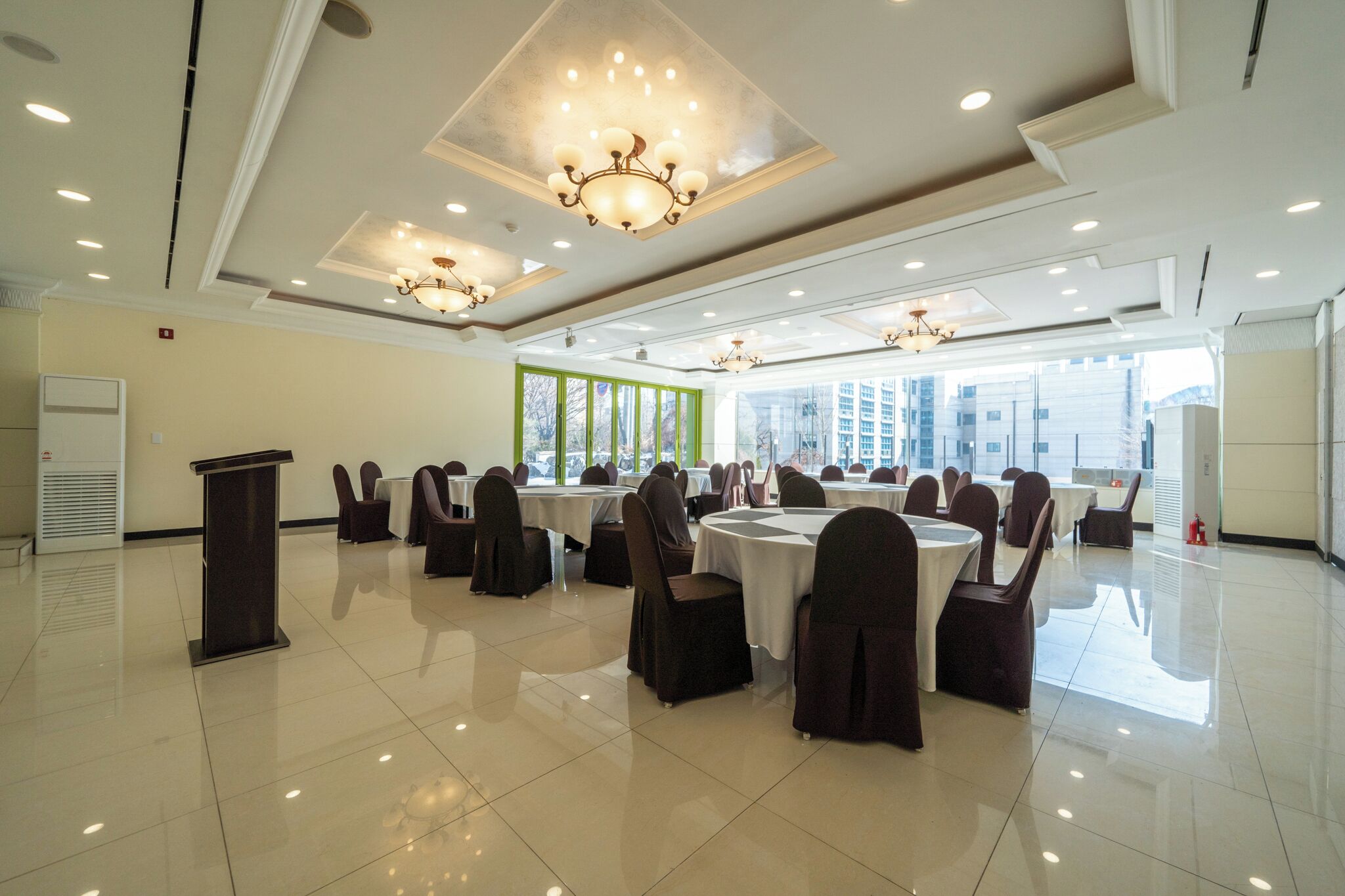 A conference room with round tables and chairs, large windows, and chandeliers.