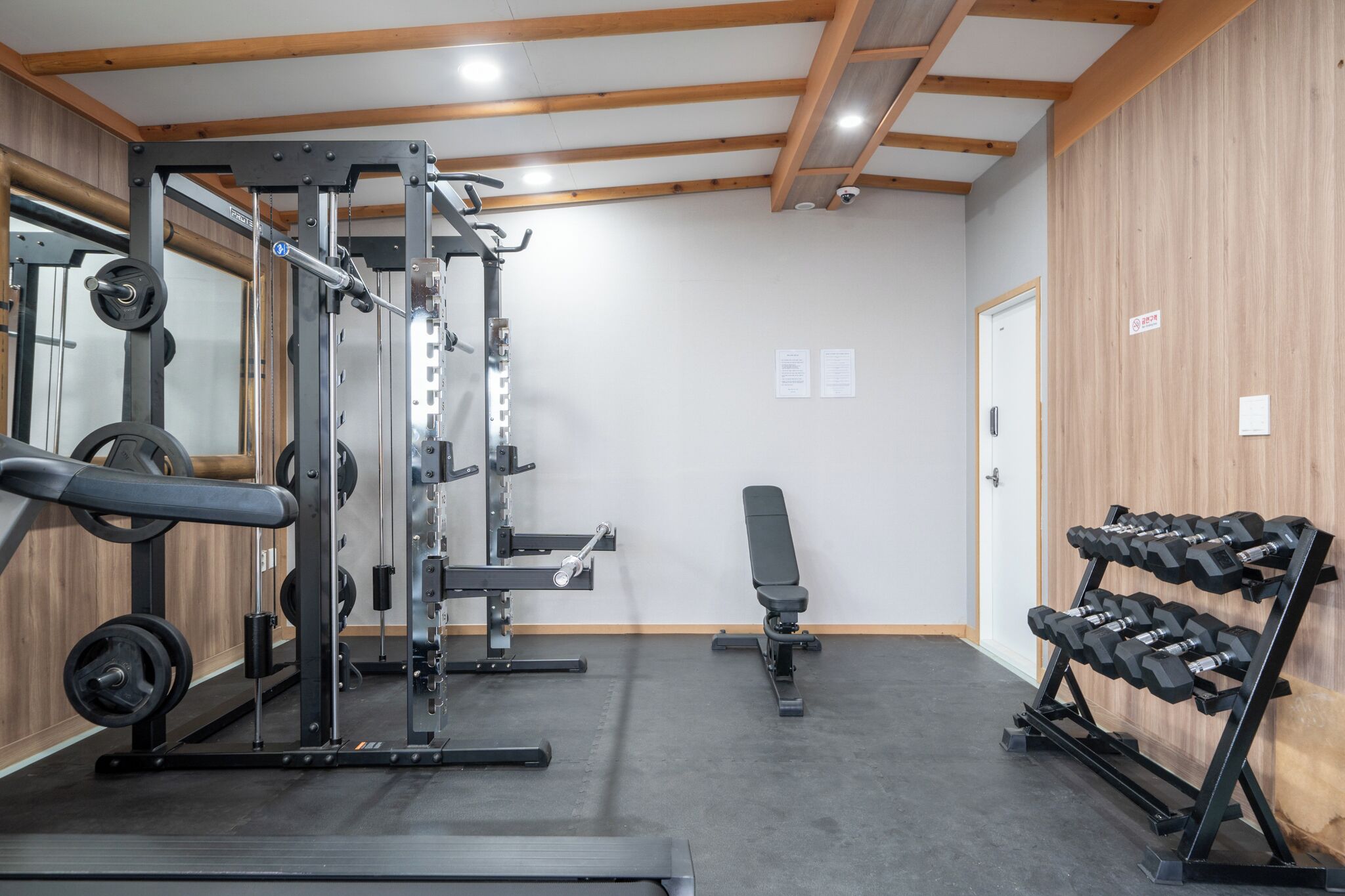 A gym with weightlifting equipment, a bench, and a rack of dumbbells.