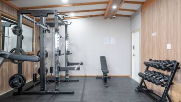 A gym with weightlifting equipment, a bench, and a rack of dumbbells.