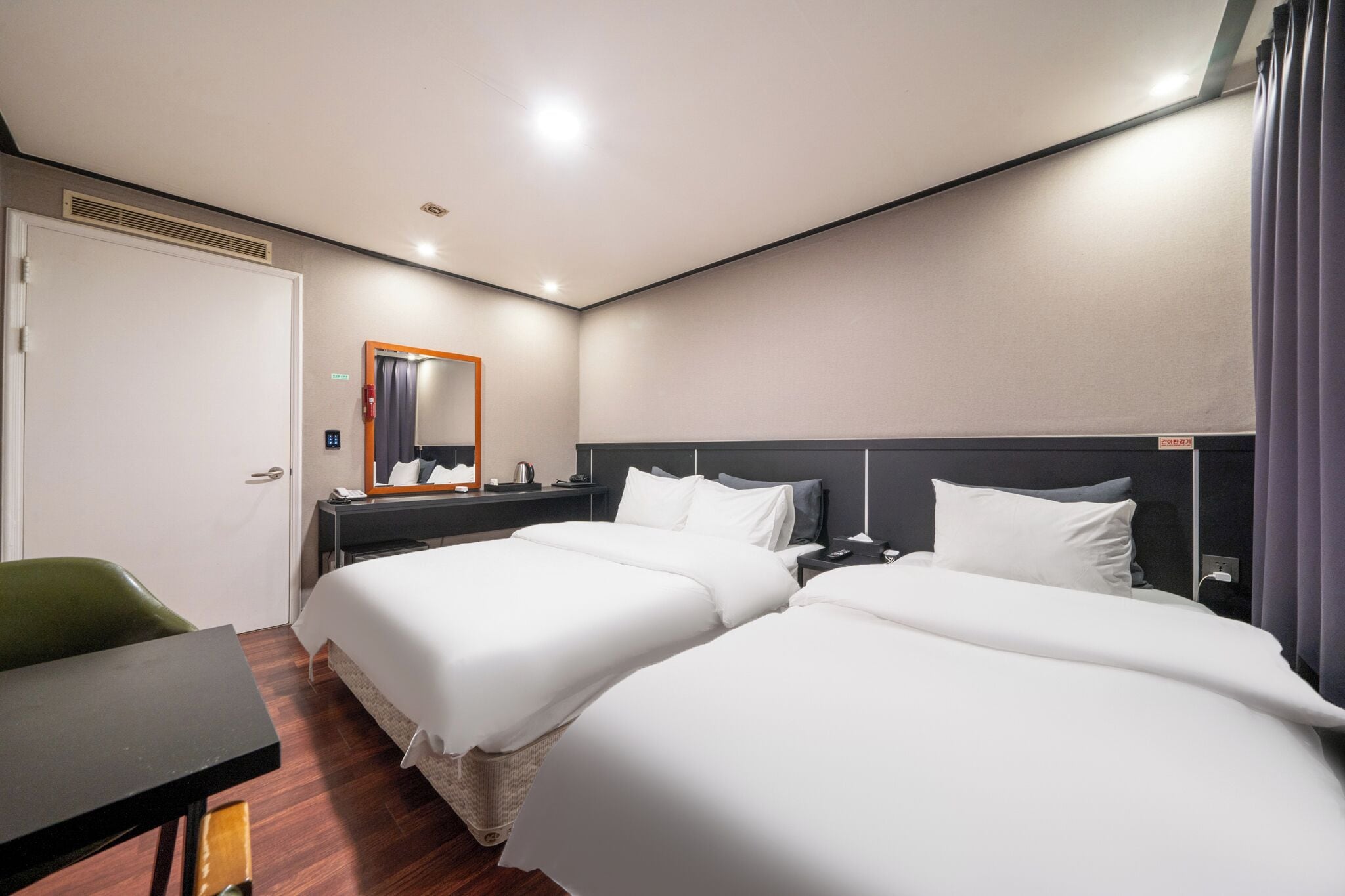 Una habitación de hotel con dos camas, un escritorio, una silla, un espejo y una puerta.