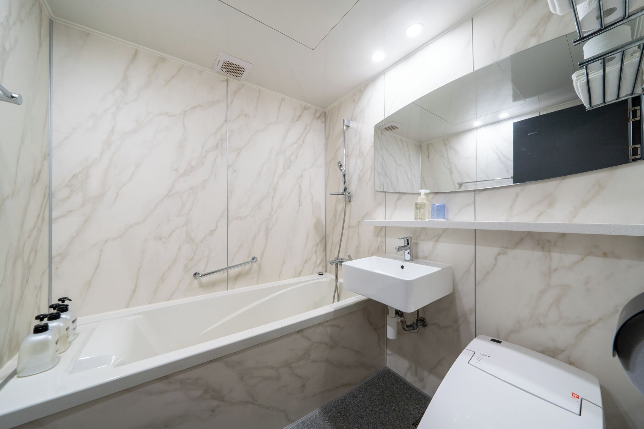 Un baño moderno con pared de mármol, una bañera, un lavabo y un inodoro.