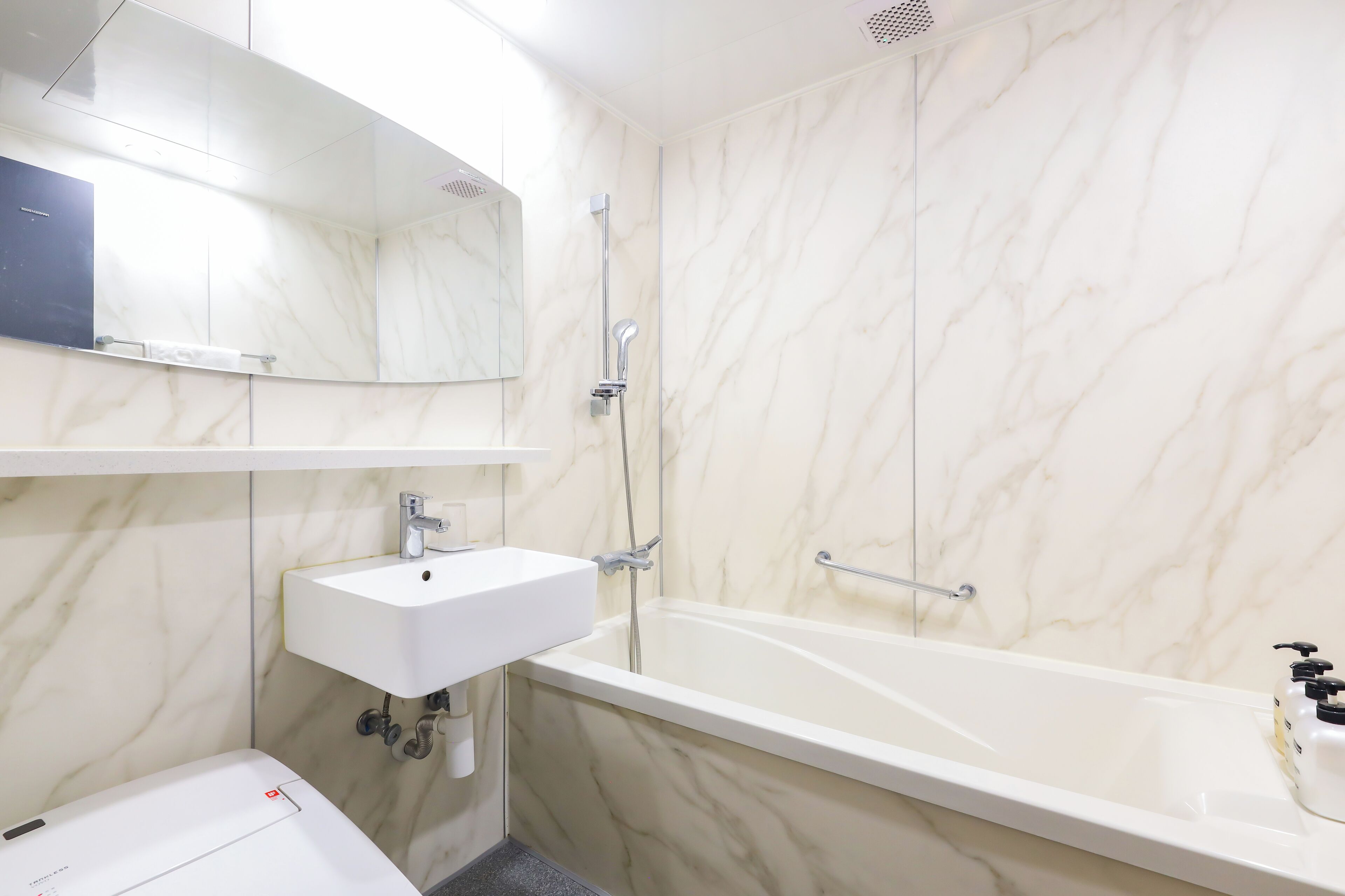 Une salle de bain avec un mur en marbre blanc, un lavabo blanc, un miroir et une baignoire.