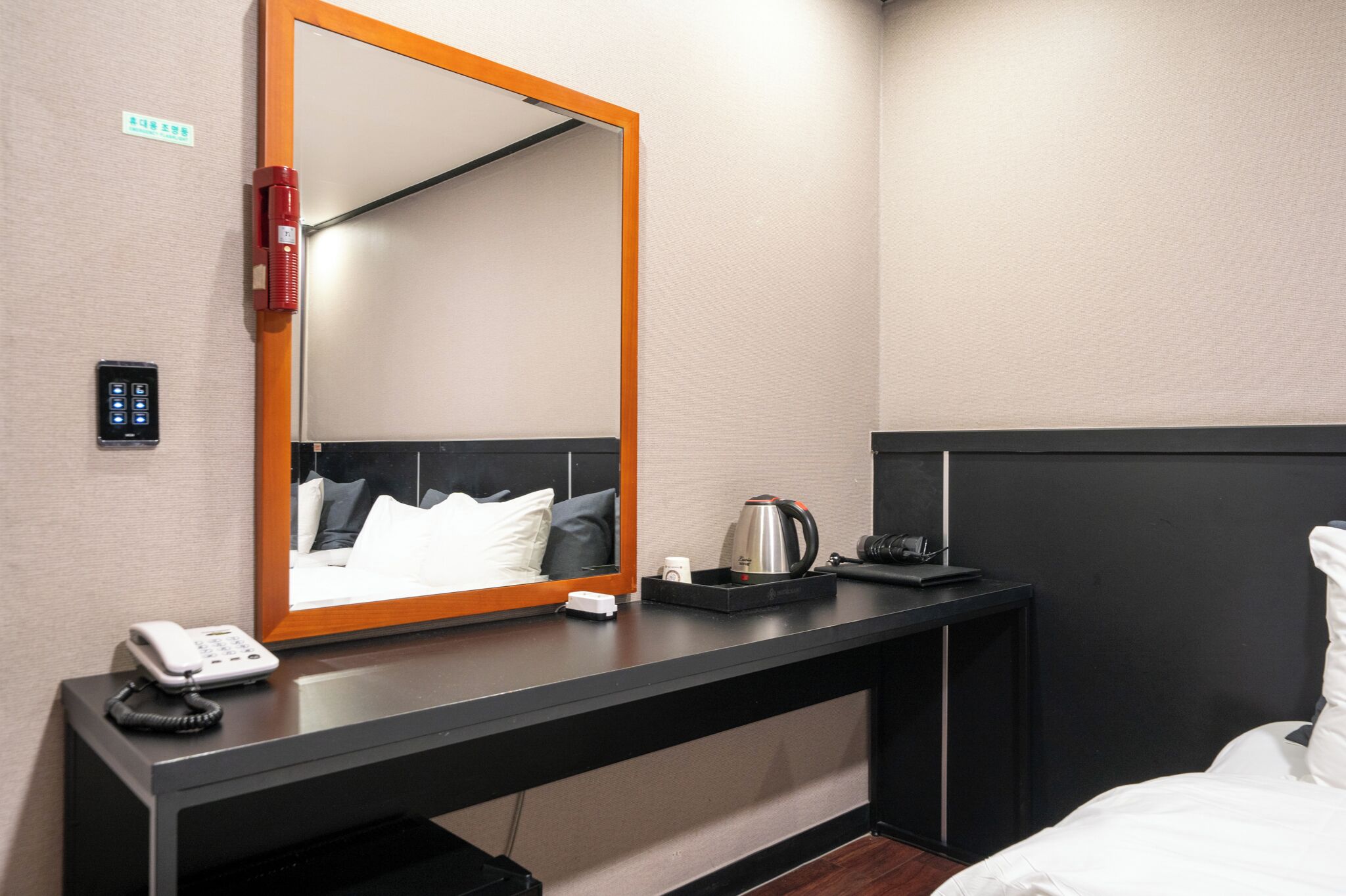 A hotel room with a large mirror, a bedside telephone, a coffee maker, and a black nightstand.