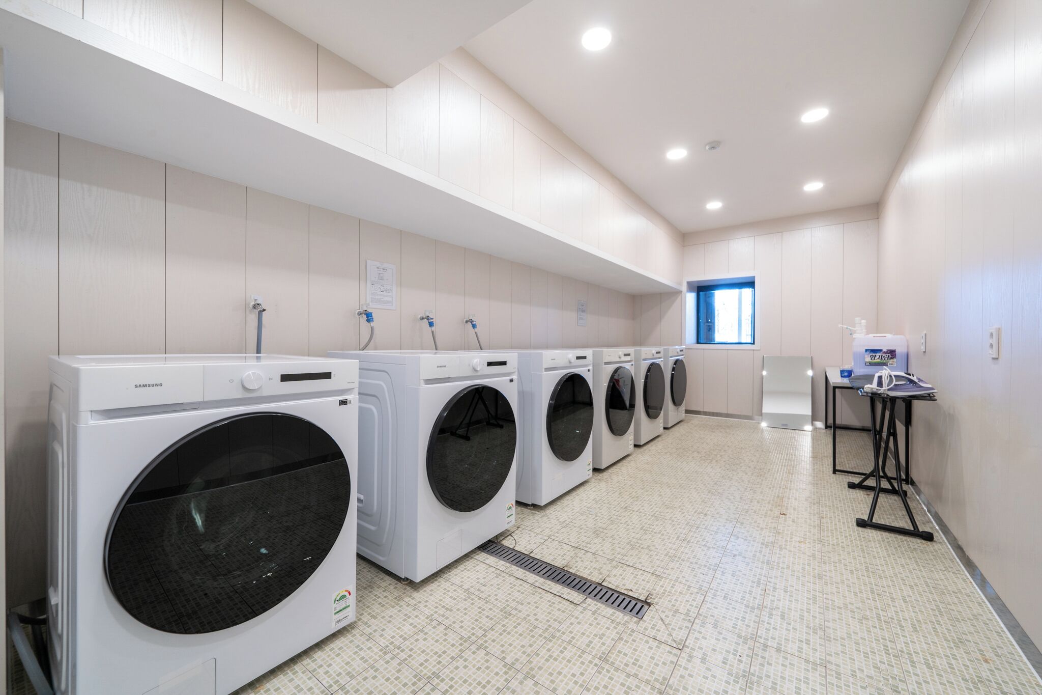 Eine Wäscherei mit mehreren Samsung Waschmaschinen, einem Lüftungssystem und einem kleinen Tisch mit Wasserspender.