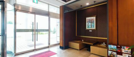 Un vestíbulo de hotel con una recepción, una zona de estar y una entrada con puerta de cristal.