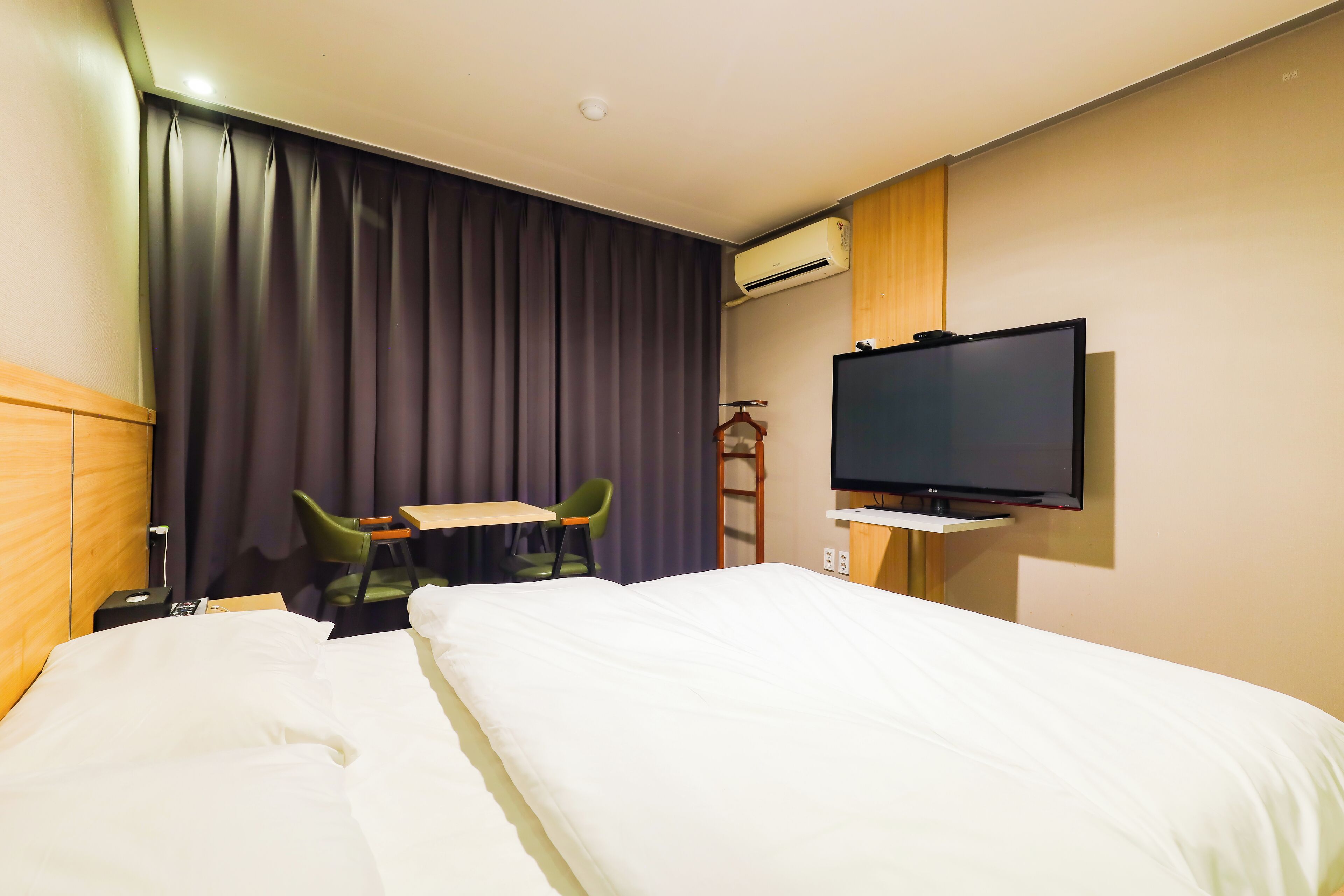 A hotel room with a bed, a desk, two chairs, a television, and an air conditioning unit.