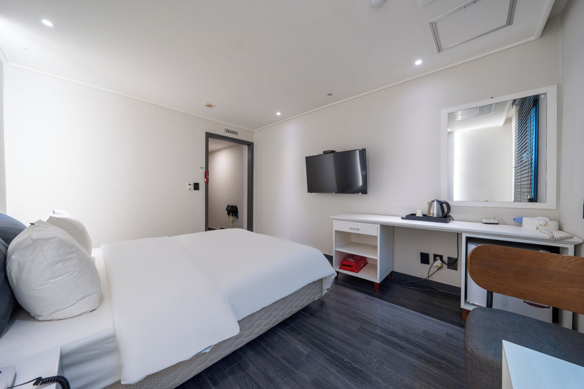 A modern hotel room with a large bed, a desk, a television, and a mirror.