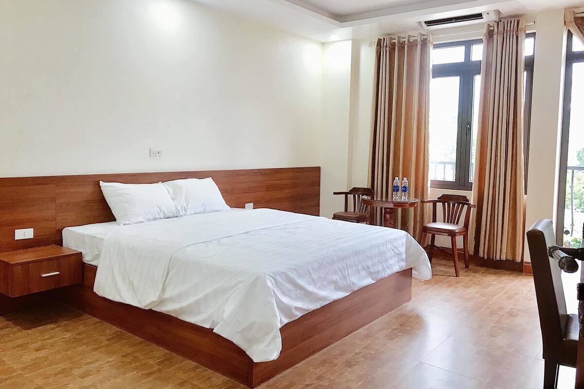 Ein Hotelzimmer mit einem großen Bett, einem Holzkopfteil, einem kleinen Tisch mit Stühlen und einem Fenster mit Vorhängen.