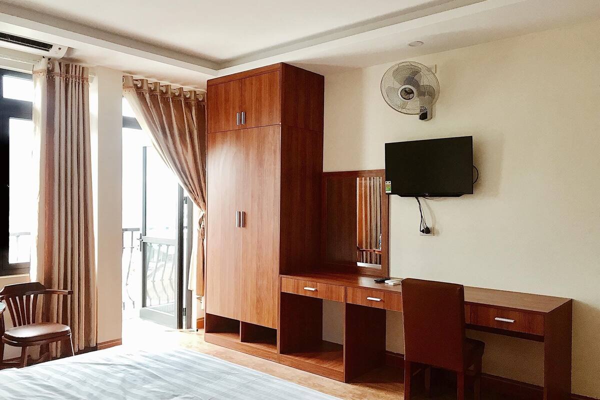 Ein Hotelzimmer mit Bett, Schreibtisch, Stuhl, Kleiderschrank, Fernseher und einem Fenster mit Vorhängen.