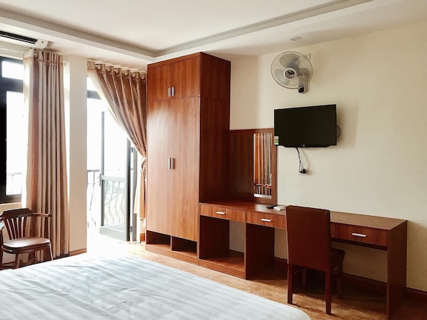 Habitación de hotel con cama, escritorio, silla, armario, televisor y ventana con cortinas.