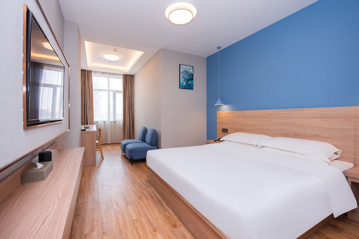 A hotel room with a large bed, a desk with a chair, a TV, and a window with curtains.