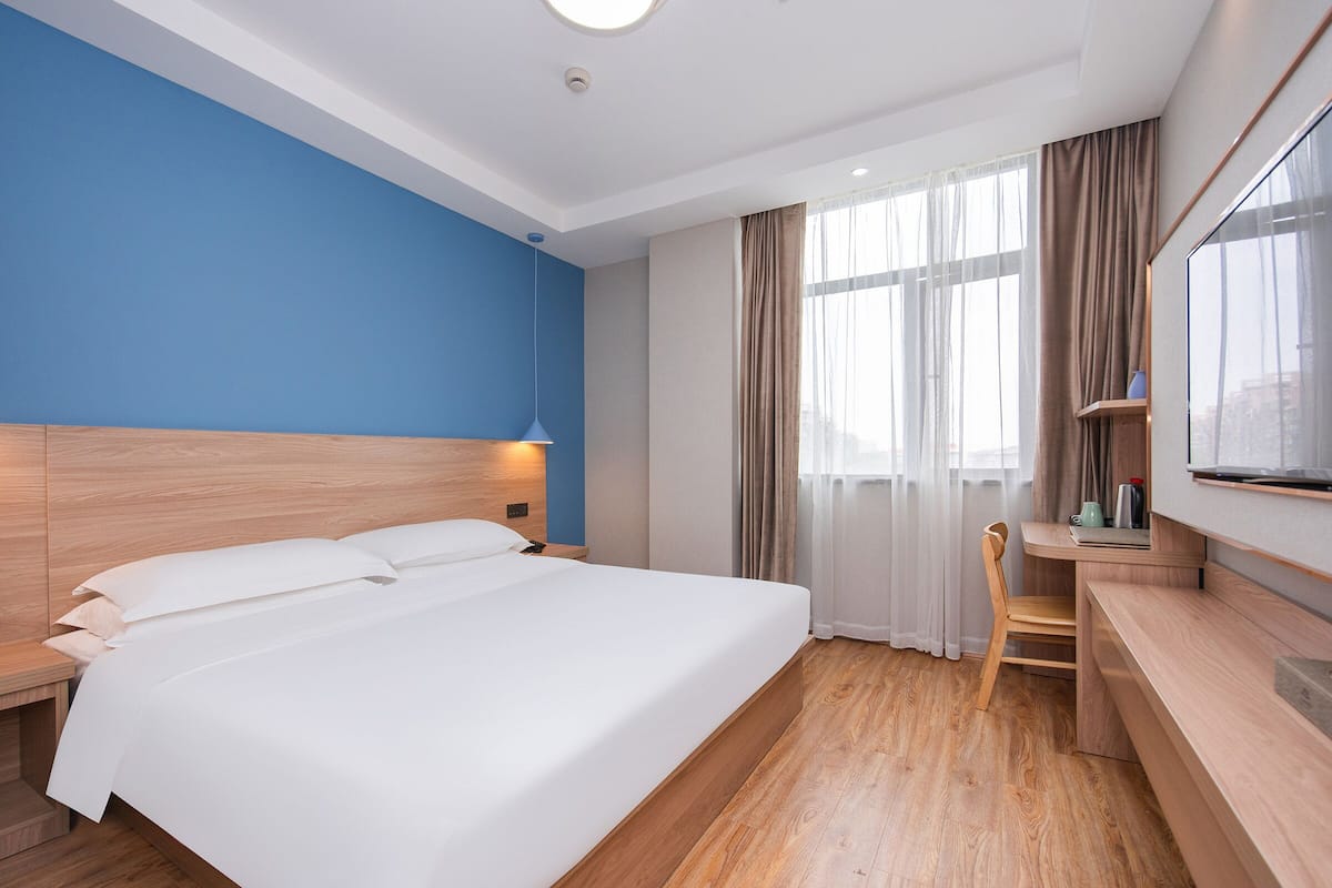 A hotel room with a large bed, a desk, and a TV.